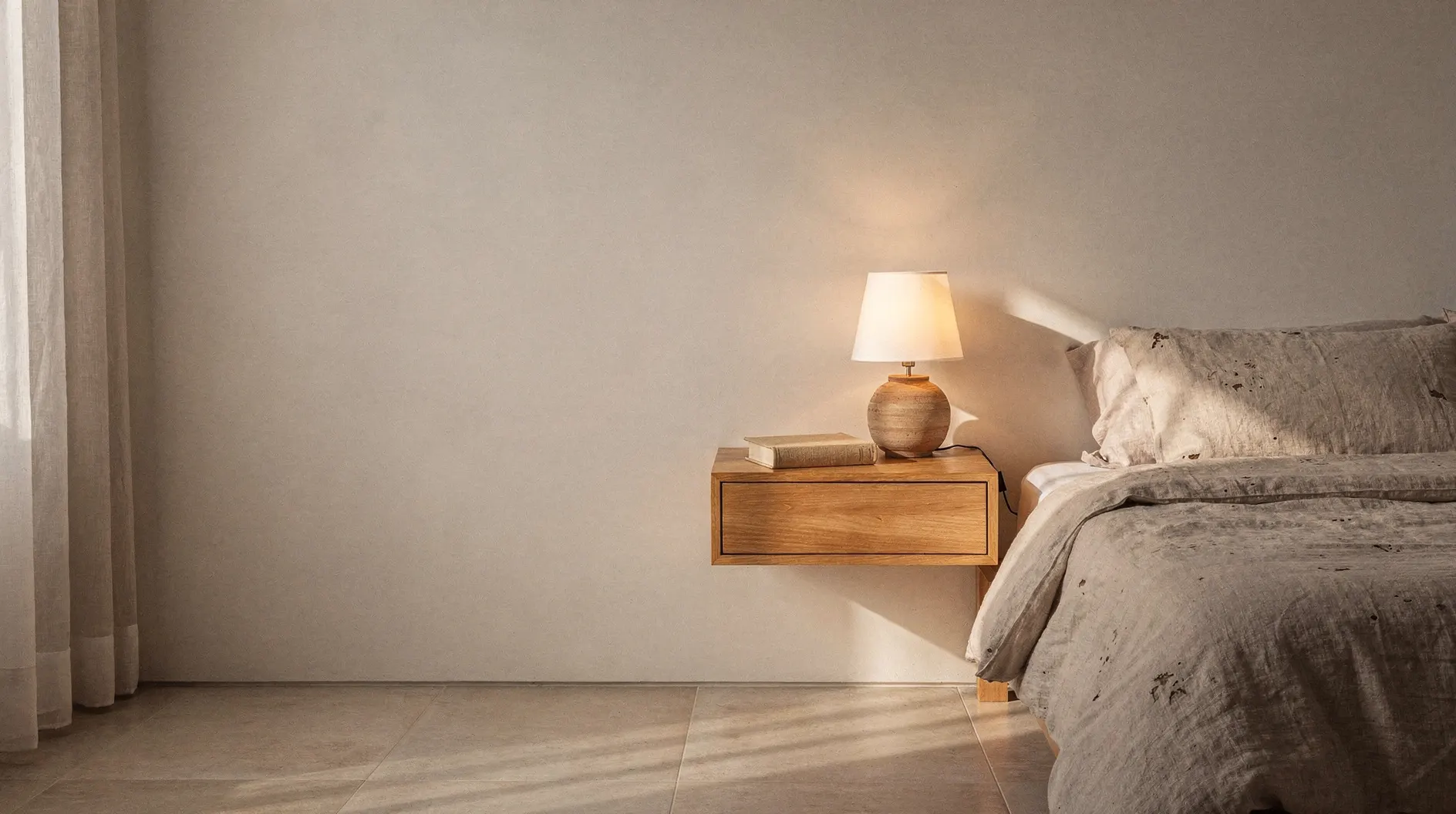 Quarto com cama de linho, mesa de cabeceira suspensa de madeira e luminária acesa.