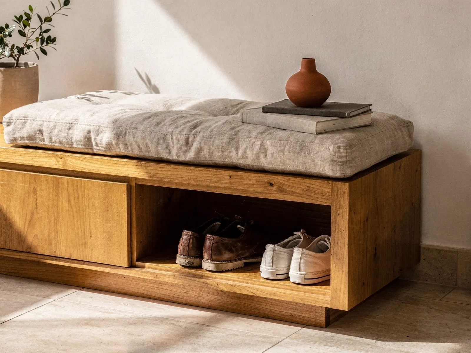 Assento de madeira maciça com almofada, sapatos nos nichos abaixo.